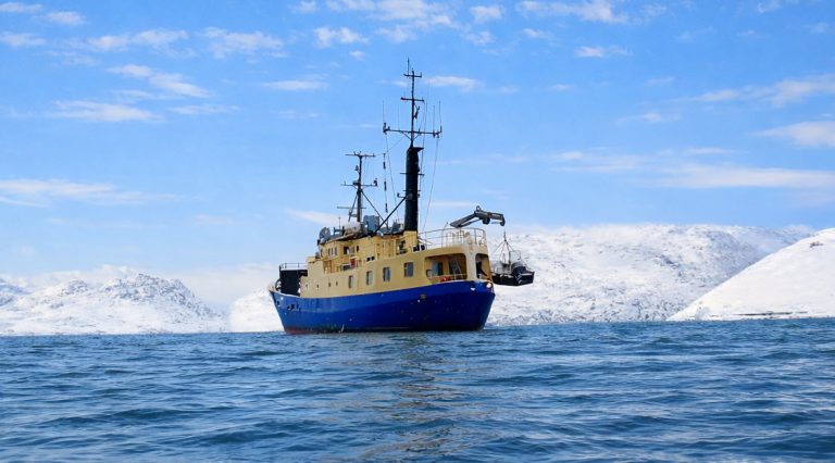 M/S Tulu expedition vessel operating in Arctic waters off the coast of Greenland, surrounded by snow-covered mountains.