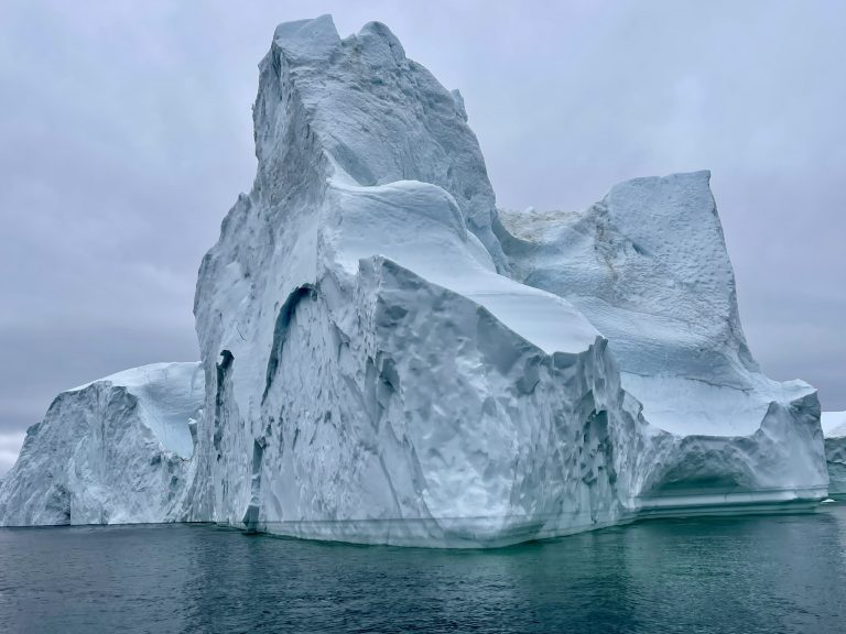 Large Arctic iceberg floating in calm water under overcast skies