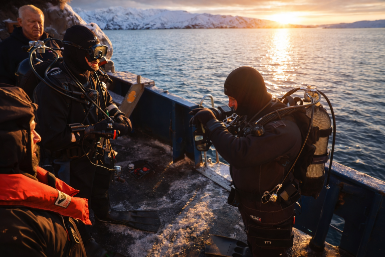 Small team of divers preparing gear on a boat in cold polar waters at sunset