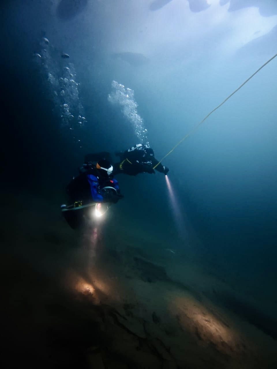 Two polar divers swimming under the ice in arctic waters