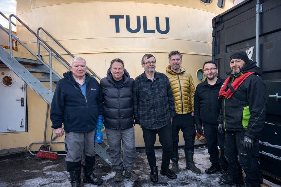 Tom Popper, Kaare Hansen, the captain, and crew standing on the main deck of the M/S Tulu in Greenland.
