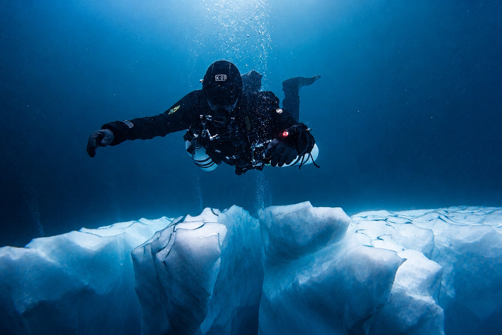A diver alongside the submerged wall of an iceberg in Greenland