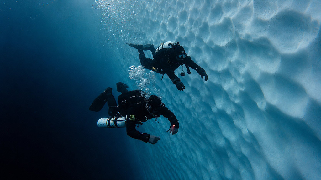 Two divers surfacing beside an iceberg in Greenland