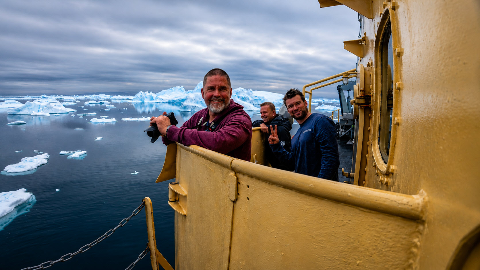 Expedition team on deck of M/S Tulu, smiling, with icebergs in the background