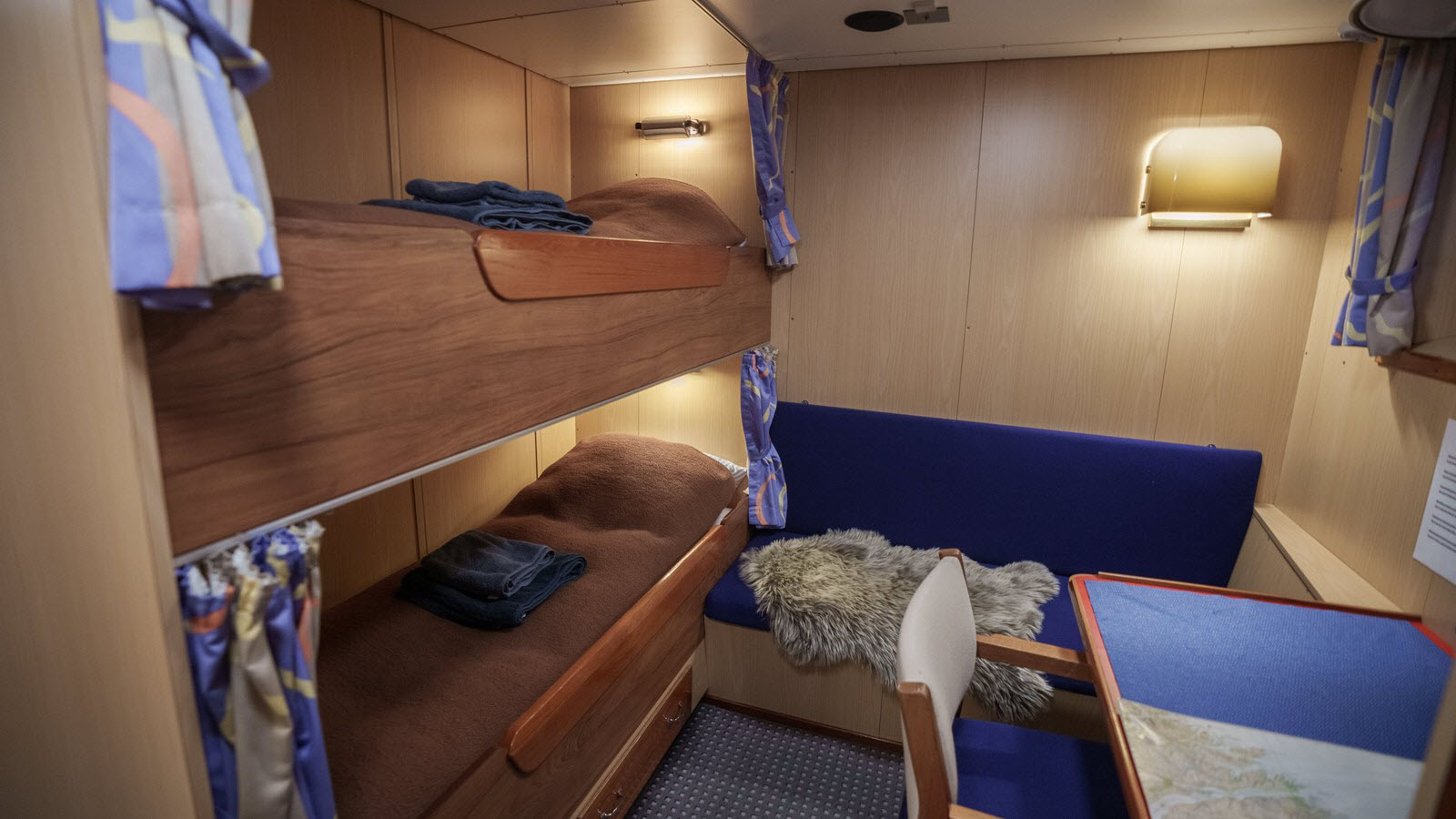 A double cabin aboard M/V Sisak with berths, a sofa, desk, and wardrobe