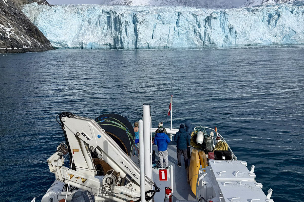 Crew and expedition gear on the working stern deck of M/V Sisak, with a crane and glacier behind, in Evighedsfjorden, Greenland