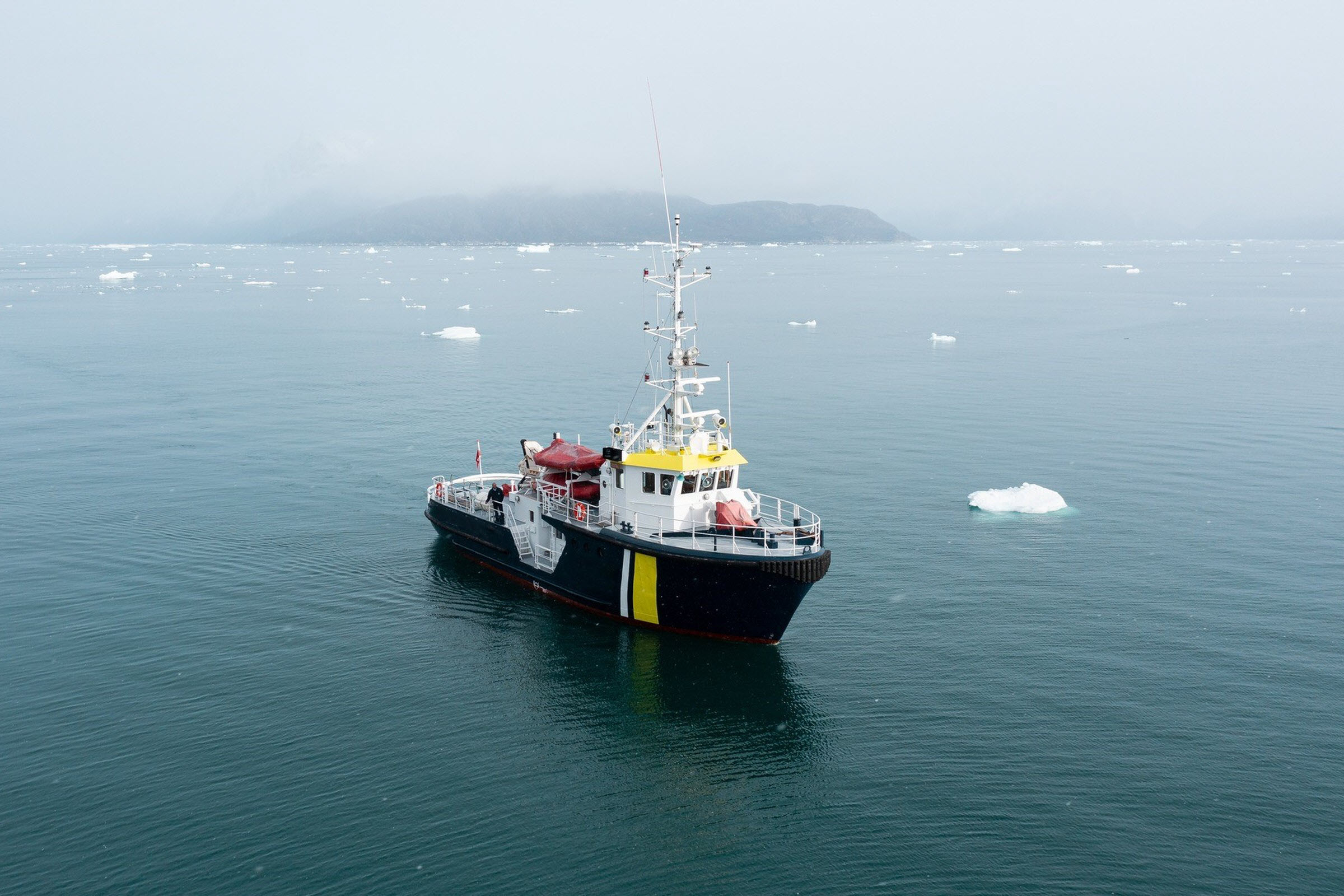 M/V Sisak at anchor in calm iceberg-flecked water off a fog-shrouded Greenland coast