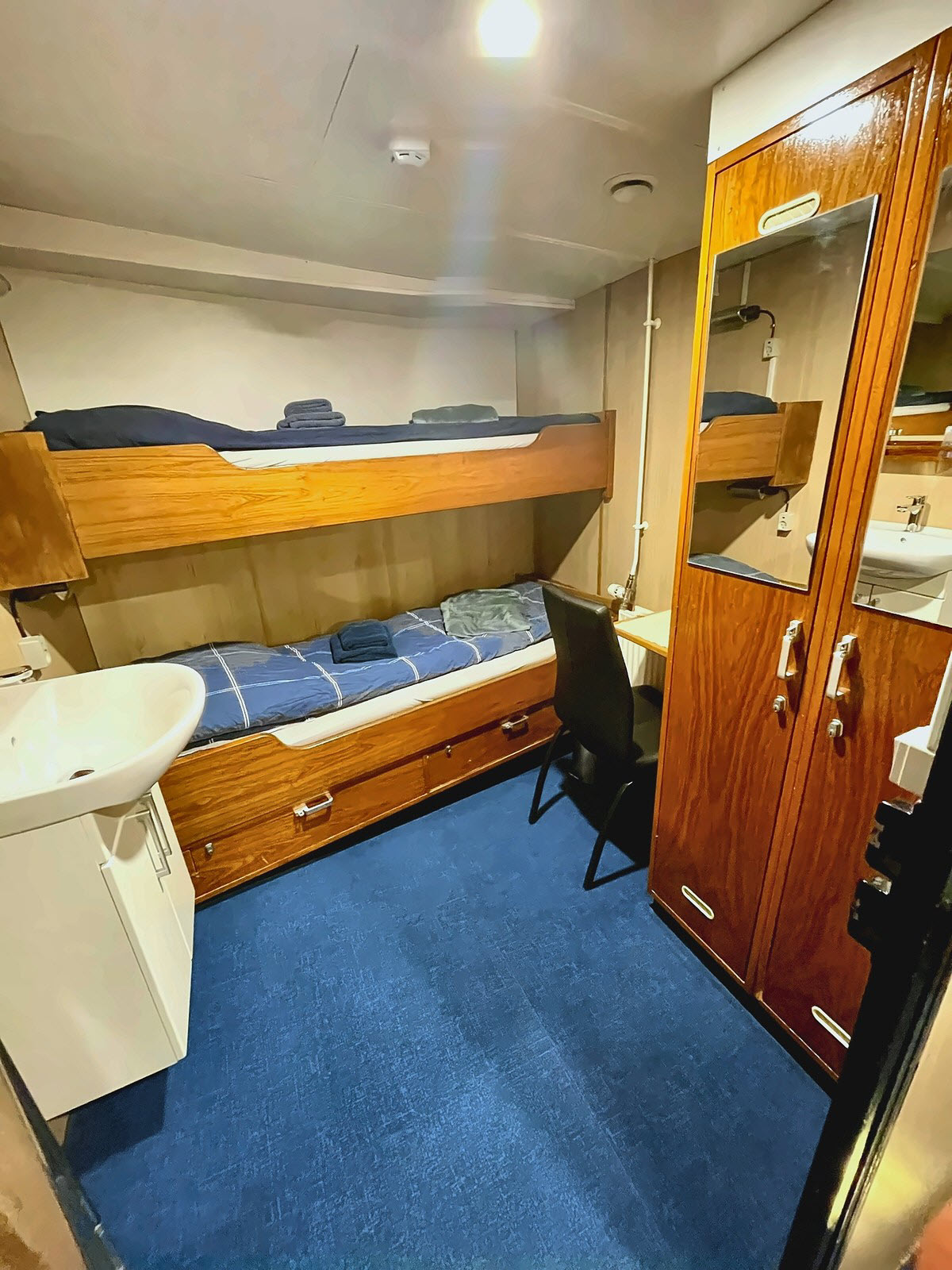A bunk cabin aboard M/S Tulu with upper and lower berths, a chart desk, sink, and wardrobe