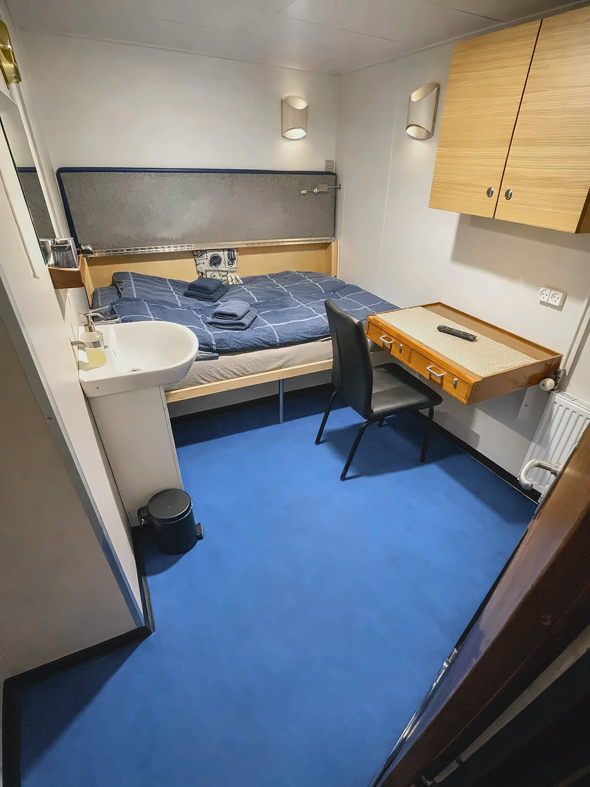 A double cabin aboard M/S Tulu with a bed, writing desk, wardrobe, and in-cabin sink
