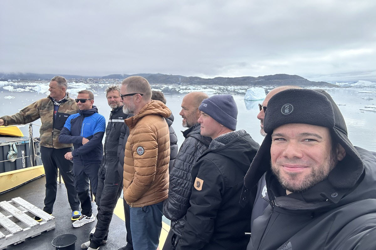 Expedition divers gathered on the deck of M/S Tulu with icebergs and Greenland's coast behind them