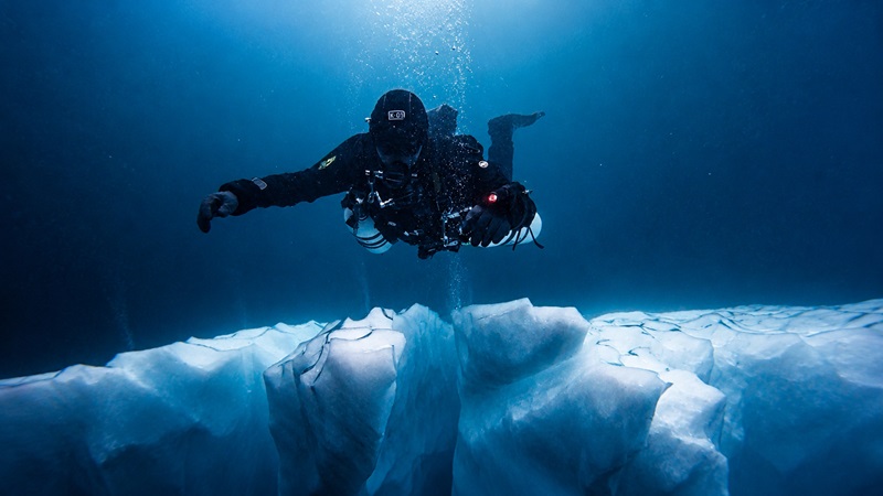 A sidemount diver swimming over the foot of an iceberg in Greenland