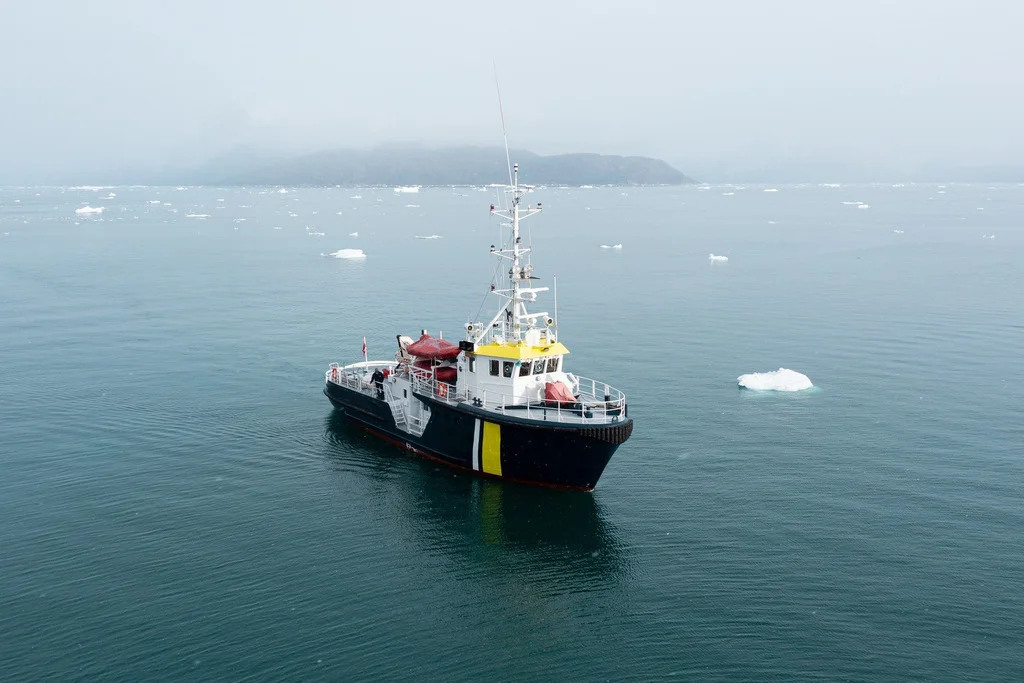 M/V Sisak at anchor in calm iceberg-flecked water off a fog-shrouded Greenland coast